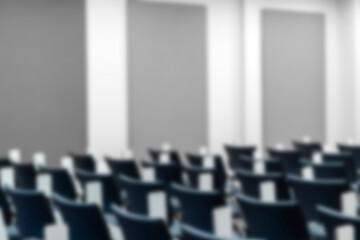 Fototapeta premium Empty blurred lecture hall with rows of blue ergonomic chairs and folding desks, ideal background for education, corporate training, academic seminars, and professional workshop presentations.