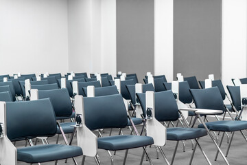 Fototapeta premium Empty modern lecture hall with rows of blue ergonomic chairs and folding desks, ideal background for education, corporate training, academic seminars, and professional workshop presentations.