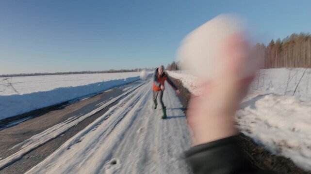 A man and a woman are playing snowballs. The guy accurately throws a snow shell at his girlfriend and runs away, and the girl catches up and throws a snowball at his back. From the first person.