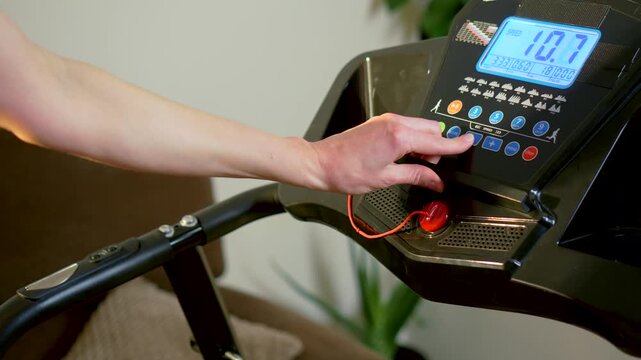 Adjusting treadmill program during active running session on home fitness machine console. Hand pressing control buttons while cardio workout continuing on electric treadmill indoors. Dynamic home