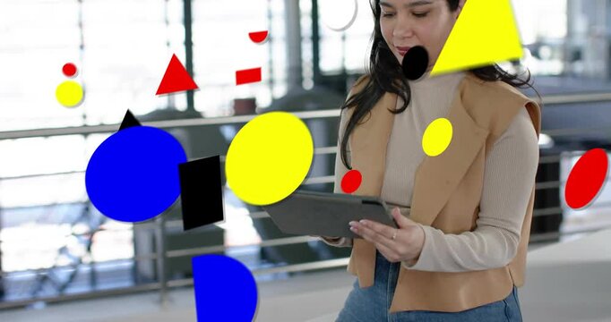 Businesswoman tapping tablet in atrium, starting graphic shapes over screen while reviewing work