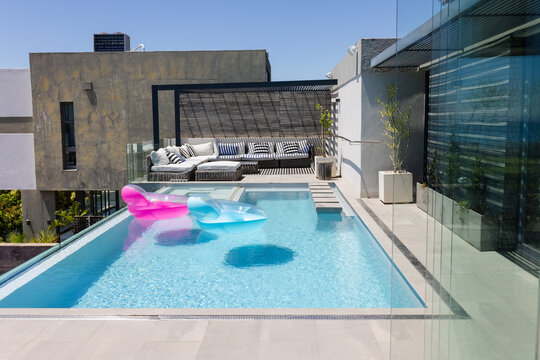 Vertical video: Casting strong sun, rooftop pool showing pink, blue loungers floating for leisure