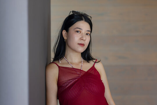 Asian woman leaning on column in hall posing in red dress sunglasses beads-and-hoops wood-wall