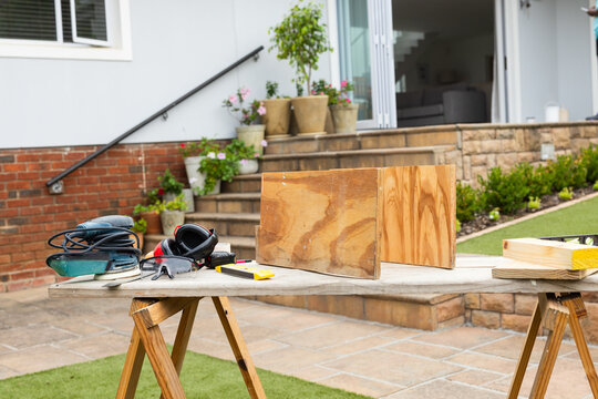 Two upright plywood panels resting on temp workbench on patio, orbital sander and goggles present