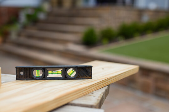 Black plastic spirit level is resting on pine plank on backyard work support, bubble vials visible