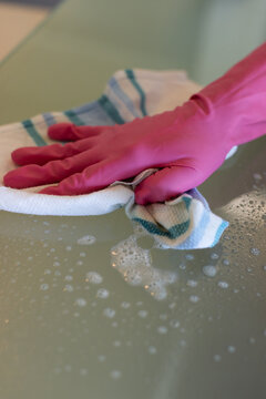 Vertical video: From soap suds, pink-gloved hand pressing teal towel on glass top, clearing bubbles