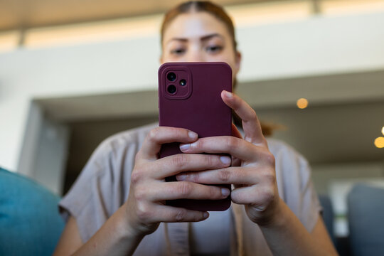 African woman wearing khaki top holding mauve phone and scrolling in lounge near teal cushion