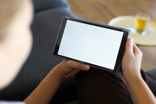 Vertical video: Settling woman in short-sleeved top holding tablet with blank white screen on sofa