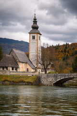Obraz premium Medieval Church of St. John the Baptist and stone bridge at Lake Bohinj in autumn, Slovenia