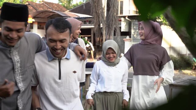 Asian friends walking together after eid, sunlit village street scene with men in caps and women in hijabs smiling and chatting,