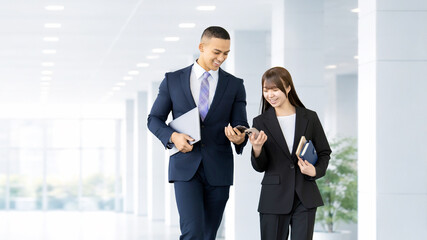 スマートフォンを見ながら歩くビジネスパーソン 男女のビジネスコミュニケーションイメージ, Business Colleagues Walking While Looking at Smartphones © Trickster*