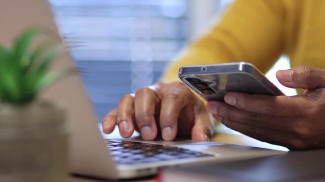 Close up of a man's hands using two factor authentication with his smartphone and laptop, showing concepts of data security, login, and password protection online