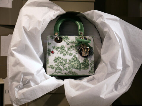 Dior boutique windows, Avenue Montaigne in Paris. 2026.  Iconic Book Tote Dior bag in "toile de Jouy", green floral pattern with chams in metal;
