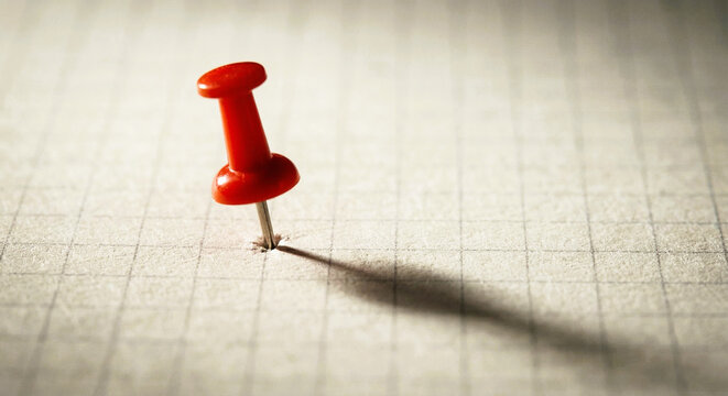 Red Push Pin Stuck Into Blank Gridded Paper Casting Shadow