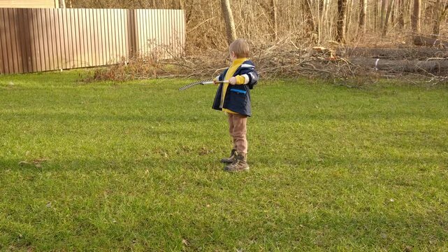 Boy Raking Up Autumn Leaves at the Home Backyard. Fall season. Seasonal garden yard work outside. Busy blonde child helps to mom gardening autumnal lawn. Cute kid learn planting. Young Raker. Chores.