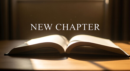 An open book lies on a wooden desk indoors with sunlight shining through.