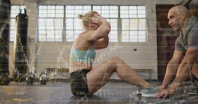 Female trainee performing sit-ups after trainer anchoring feet, financial chart overlaying subjects
