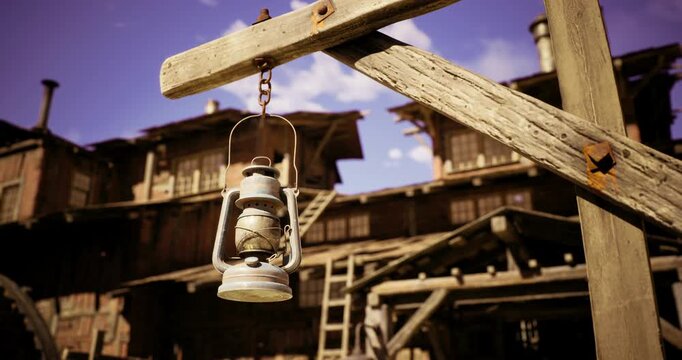 A vintage lantern dangles from a wooden post in front of an aged wooden building. The clear sky enhances the rustic charm of the historical setting, evoking feelings of nostalgia.
