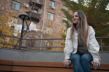 Fototapeta premium Mid adult woman sitting on bench in park in evening