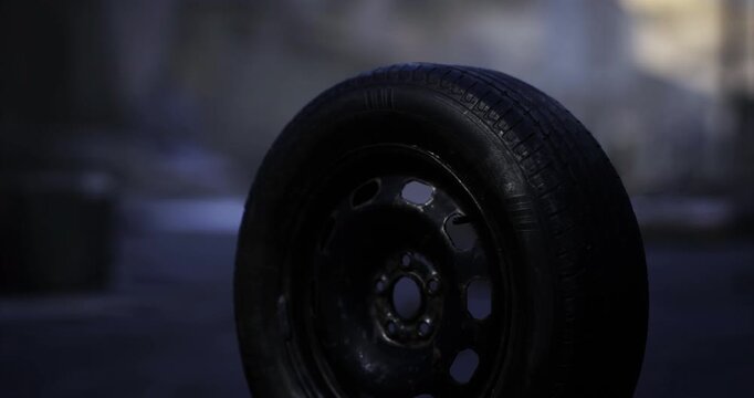 A solitary black tire rests on a desolate urban street, surrounded by debris. The environment appears damp and gloomy, hinting at recent heavy rain or a storm.