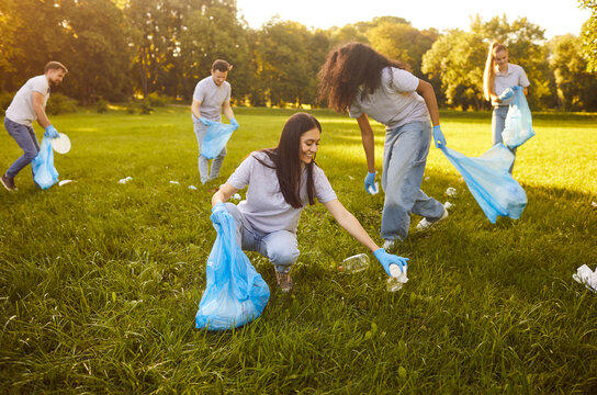 Group happy volunteers participating in environmental clean up day, working together in green park, picking litter collecting garbage, friends community members actively engaging environment cleaner
