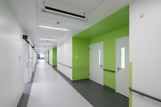 Modern hospital corridor interior with elevators and emergency exit signs.