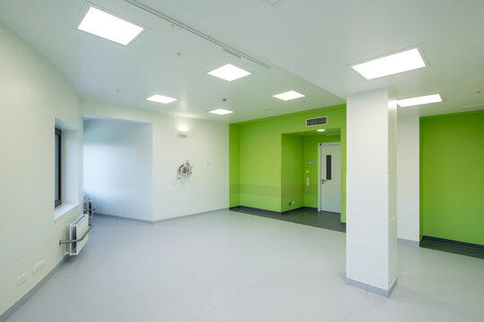 Modern hospital corridor interior with elevators and emergency exit signs.