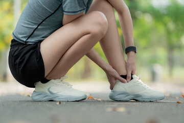 Young woman suffering ankle pain after running in park, squatting and holding injured foot, sports injury and sprained ankle outdoor fitness concept. workout, foot, sprain, strain, ankle, pain, injury © Thitiporn