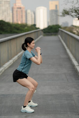 Fototapeta premium Young woman doing squat exercise on urban bridge, outdoor fitness training, strength workout, healthy lifestyle, active city living and bodyweight workout concept. woman, squat, workout,