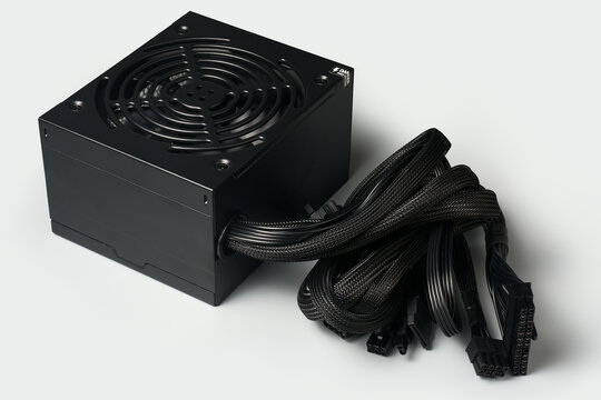 black atx pc power supply unit with cooling fan and bundled cables isolated light gray background, computer hardware electrical component, angle view