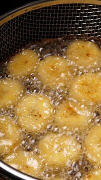 Cooking fried bananas in fryer fat. Closeup. Vertical footage