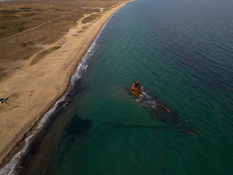 Aerial view of a sunken shipwreck near Epanomi beach, Thessaloniki, Greece. Old rusty vessel in turquoise Mediterranean water surrounded by sand and sea textures, dramatic coastal landscape.