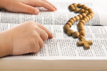 Christian wooden cross with child hand on Bible