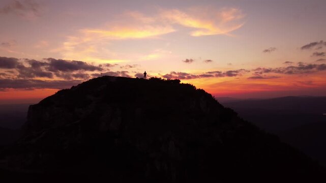 Aerial view, silhouette of a man standing on a mountain peak at sunset