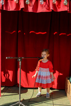 Little girl singing into microphone on small outdoor stage childhood talent concept