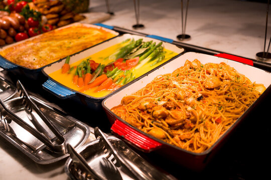 Three hot dishes served on a buffet counter with detailed plating and fresh ingredients