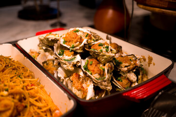 Grilled oysters topped with chopped green onions served in a red ceramic dish