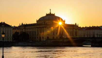 Obraz premium The sun sets behind a grand building, illuminating its architectural details. The river reflects the warm colors of the sunset and the peaceful surroundings.