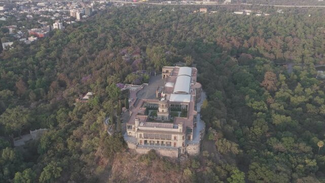 Aerial panoramic view over Chapultepec Forest and Chapultepec Castle in Mexico City at sunrise, surrounded by dense green woodland with a Ferris wheel in the distance