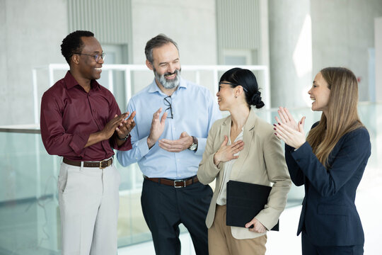 Happy business professionals applauding and recognizing a colleague for her great work and success in a modern office
