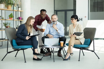 Fototapeta premium Diverse business people gathering around laptop, discussing ideas and collaborating on project in modern office lounge