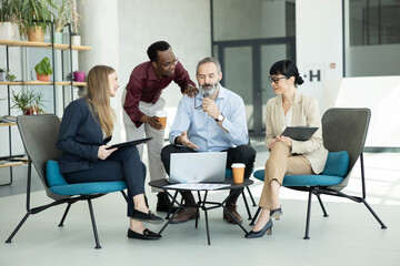 Fototapeta premium Four multi-ethnic business colleagues having an informal meeting in a modern office lounge, discussing work using a laptop