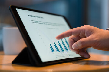 A man's finger touches a tablet screen displaying market report charts and data visualization