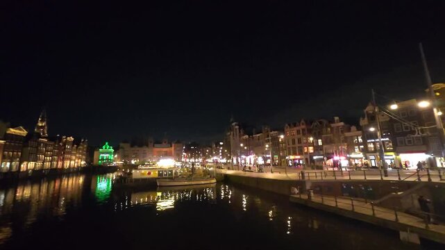 Bright streetlights are reflected in the waters of the Damrak channel in the hear of Amsterdam at Night.