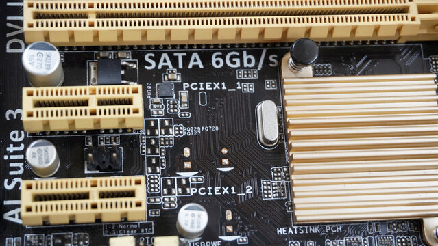 Close-up of computer motherboard circuit board showing SATA and PCIe slots, capacitors, and detailed electronic components.