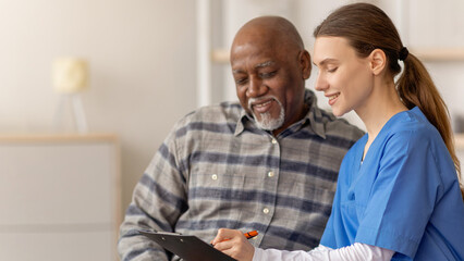 Healthcare worker sits with an older man in a medical office. The worker discusses important...