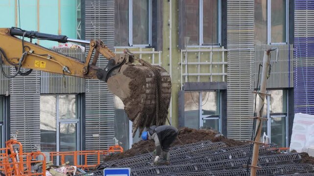 The excavator uses a bucket on metal chains to carry the metal mounting structure. 