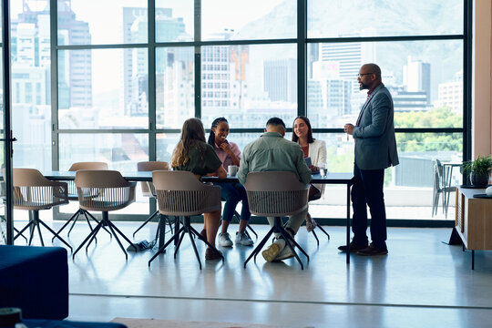 Mature businessman presenting to team during meeting in boardroom with city view at office