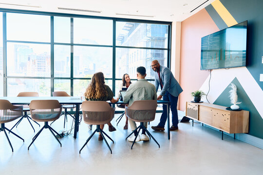 Businessman discussing with team during meeting in boardroom with large windows at office during daytime