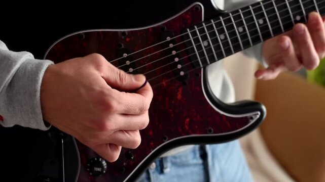 Strumming electric bass guitar. Musician plays music. Man fingers holding mediator. Man hand playing guitar neck in dark room